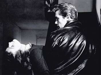 A man in a leather jacket holding a woman in a dramatic black and white scene.