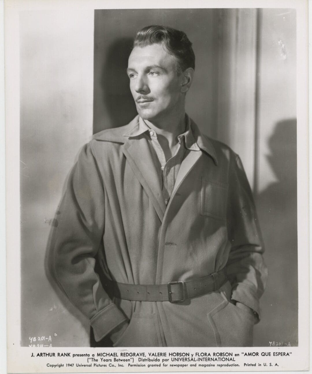 Black and white portrait of a man in a belted trench coat.