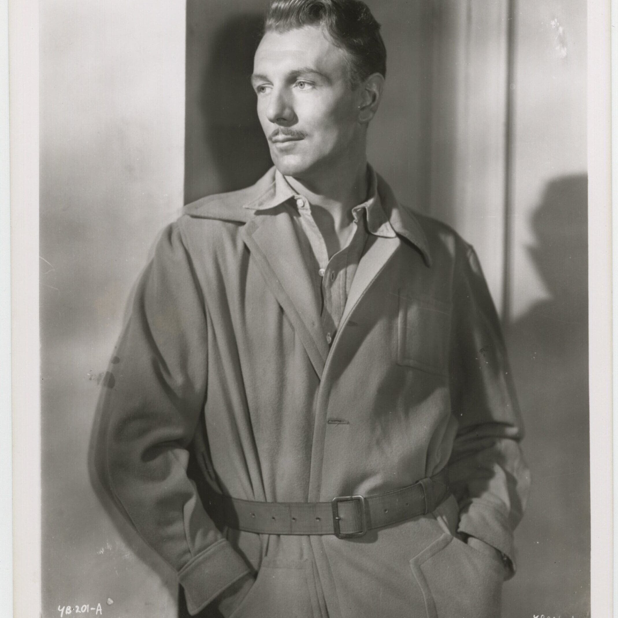 Black and white portrait of a man in a belted trench coat.